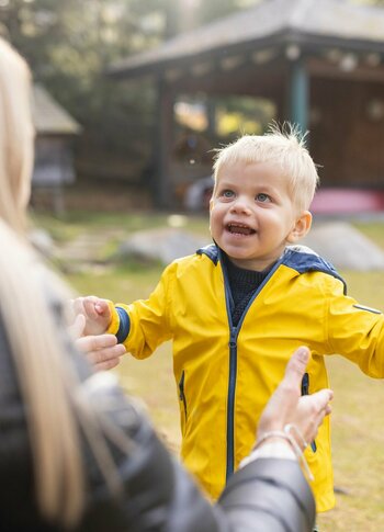 Familienurlaub im Herbst auf der Turracher Höhe Ein Kleinkind in gelber Jacke läuft einer Frau im Garten entgegen, im Hintergrund steht ein Pavillon.