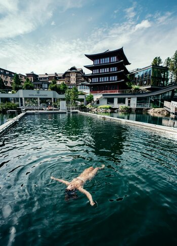 Beheiztes See-Bad am Hotel Hochschober Eine Person schwimmt entspannt im beheizten See-Bad vor dem Hotel Hochschober unter blauem Himmel.