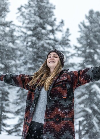 Winterfreude beim Schneespaziergang auf der Turracher Höhe Eine Frau steht mit ausgebreiteten Armen im Schnee vor verschneiten Tannen.