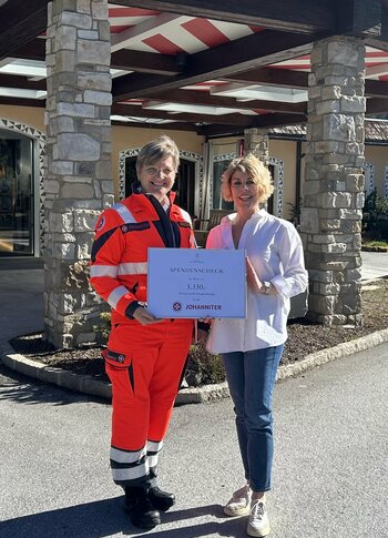 Mitten in Kärnten Hotel am See. 4-Sterne-Superior-Genuss Vor dem Hotel Hochschober übergeben Karin Leeb und eine Vertreterin der Johanniter symbolisch den Spendenscheck über 3.330 Euro. Die Spendensumme wurde gemeinsam mit den Gästen durch gesammeltes Skipfand ermöglicht und anschließend verdoppelt.