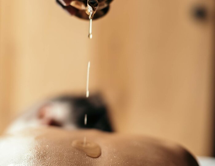 Abhyanga with Shirodhara at Kristall Spa A hand pours warm oil onto the back of a reclining person during an Abhyanga massage with Shirodhara.