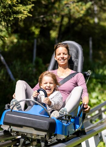 Sommerrodelbahn auf der Turracher Höhe Eine Frau und ein Kind fahren gemeinsam auf einer Sommerrodelbahn durch die grüne Berglandschaft.