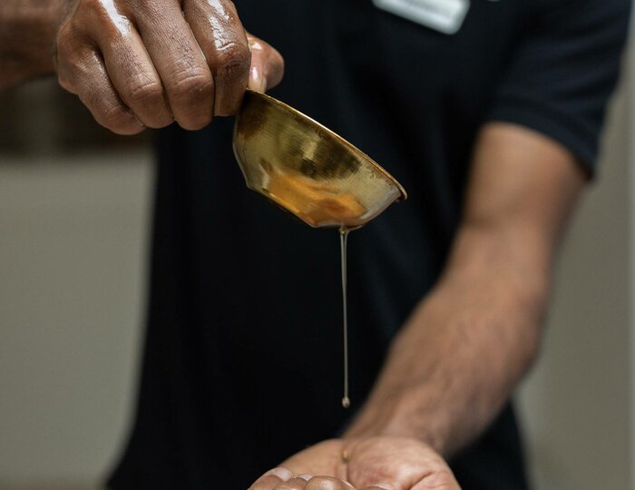 Nabhi Prishta Treatment at Kristall Spa A therapist pours warm oil from a bowl onto the abdomen of a person lying down during a Nabhi Prishta treatment.