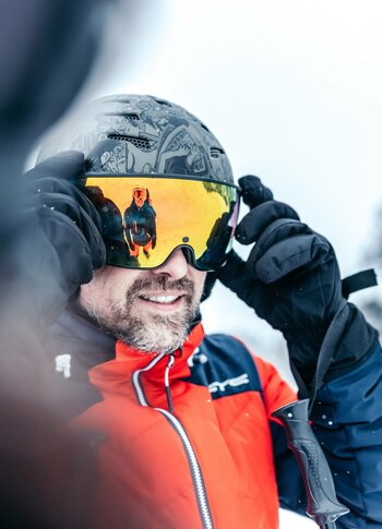 Skiurlaub mit Skifahrer am Hotel Hochschober Ein Skifahrer richtet seine Skibrille und trägt eine rote Jacke sowie Handschuhe im Schnee.