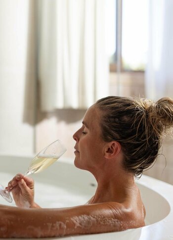 Badezimmer mit Badewanne, Frau badet und trinkt Champagner. Frau liegt in einer Badewanne mit Schaum und trinkt Champagner.
