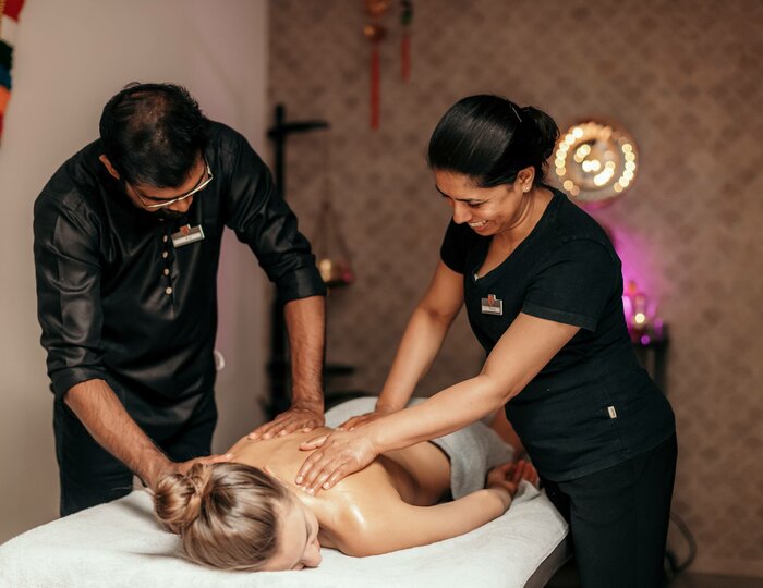 Abhyanga Royal massage at Kristall Spa Two spa staff members perform an Abhyanga Royal massage on a person lying on a treatment table in the Kristall Spa.