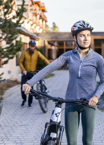 E-bike rental at Hotel Hochschober A woman wearing a helmet stands with an e-bike in the hotel courtyard, while a man walks a bike behind her.